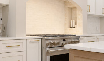 Modern white kitchen with stainless steel stove and built-in cabinetry, featuring a cozy archway and.