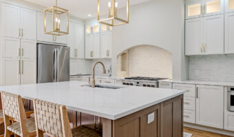 Modern white kitchen with large island, stainless steel appliances, and elegant lighting fixtures. P.