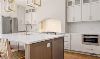 Modern white kitchen with an island, gold pendant lights, and wooden flooring, showcasing home renov.