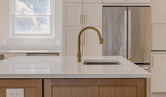 Modern kitchen with white cabinets, gold fixtures, and a central island featuring a built-in sink. B.