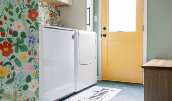 Washer and dryer in a colorful laundry room with floral wallpaper and a yellow door.
